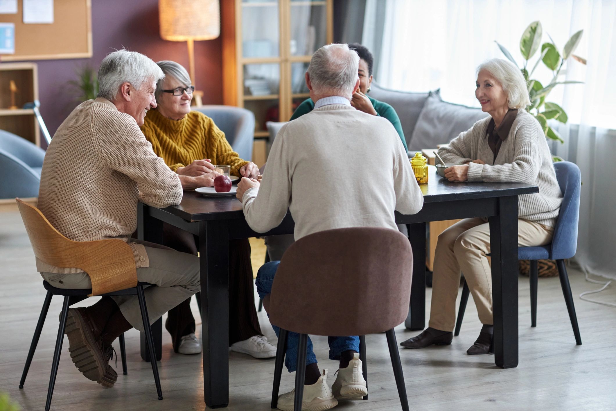 Seniors sitting together at a table and smiling in a care home common room