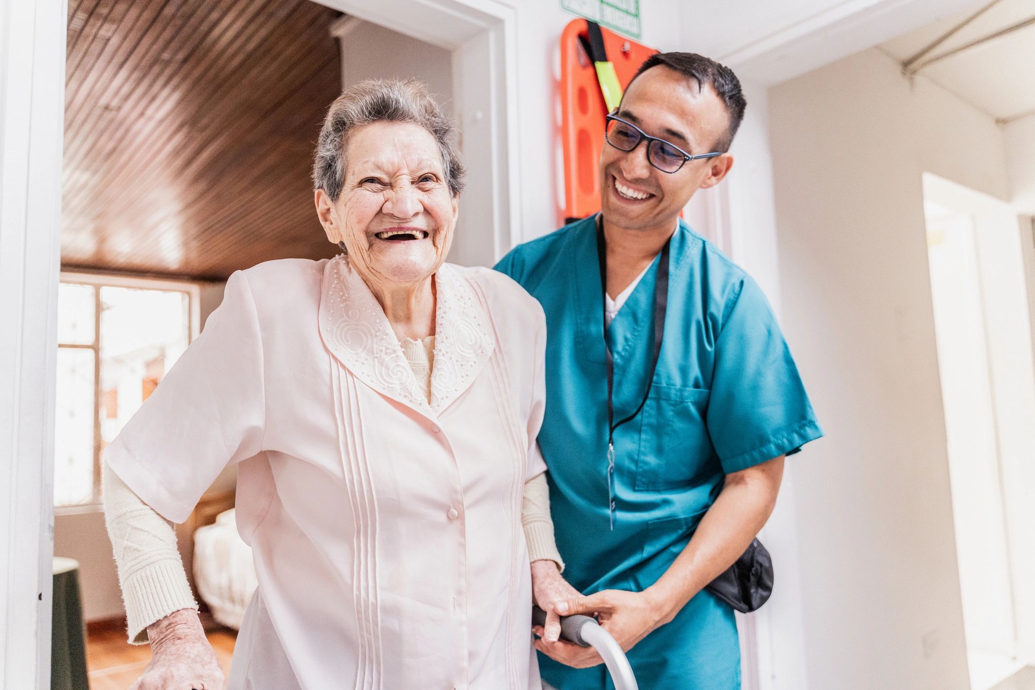 Caregiver supporting a senior woman walking with a walker indoors